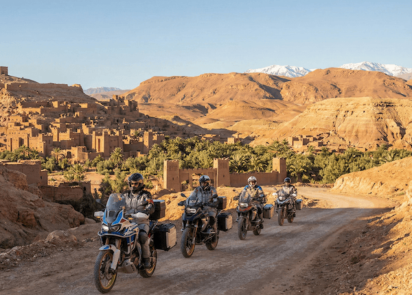 Riders on a gravel road below the snow-capped Atlas Mountains in Morocco