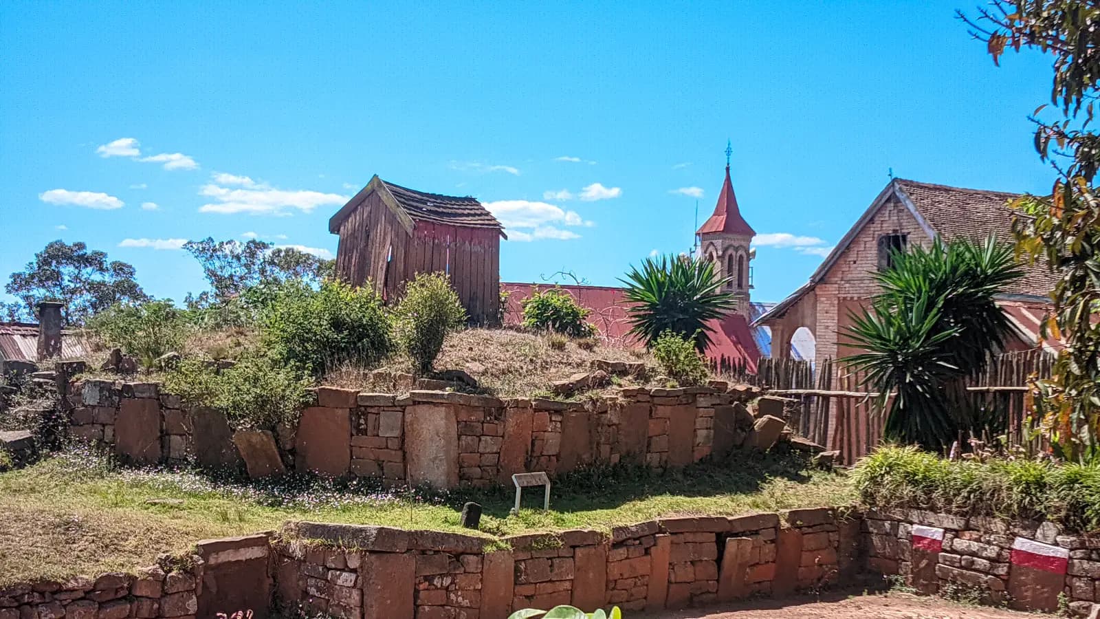 Stone walls and terraces in the village of Ambohidrabiby, with a wooden house and a church tower behind