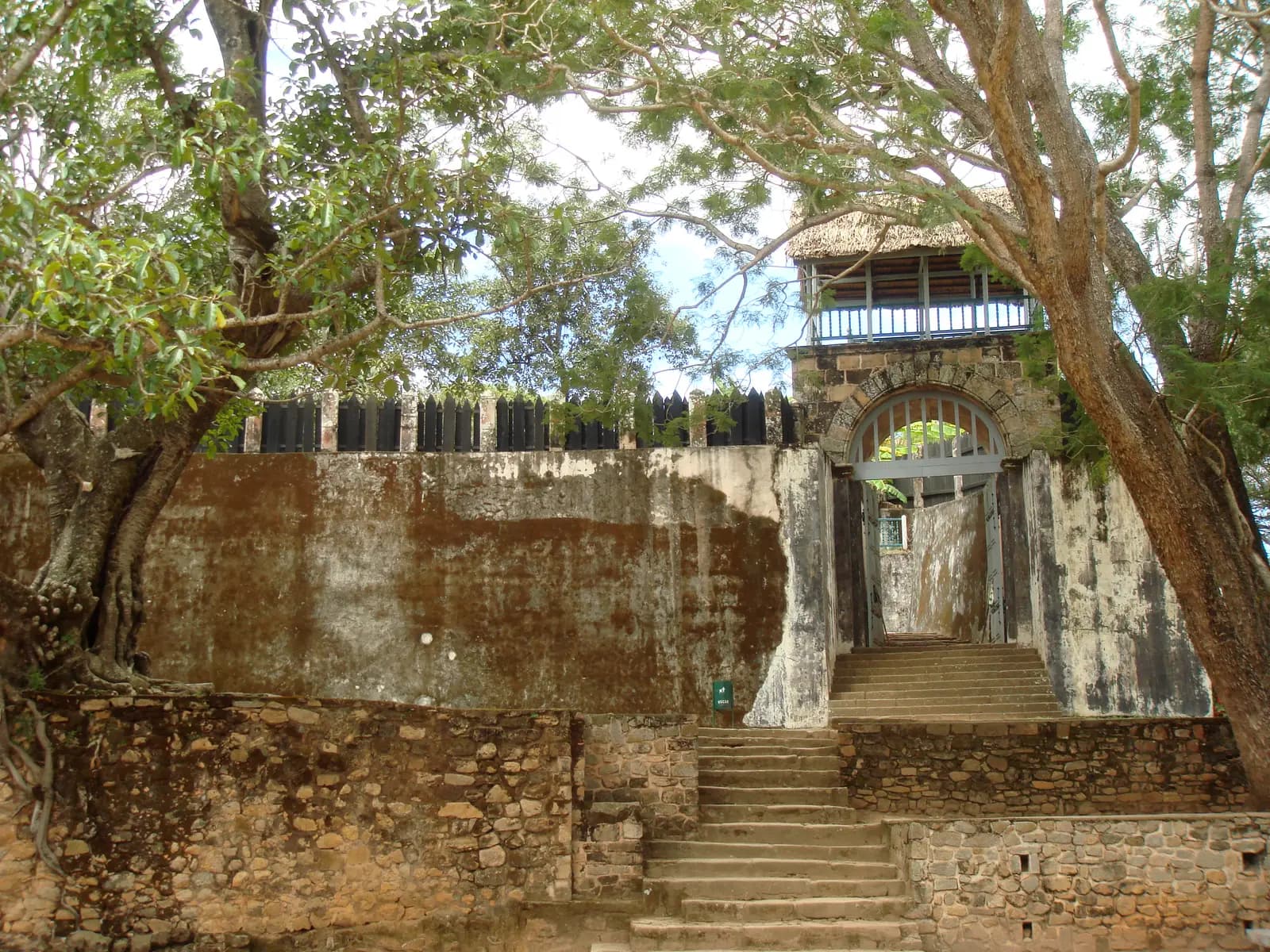 Stone steps leading up to a gate in the wall of the royal compound at Ambohimanga, under large trees
