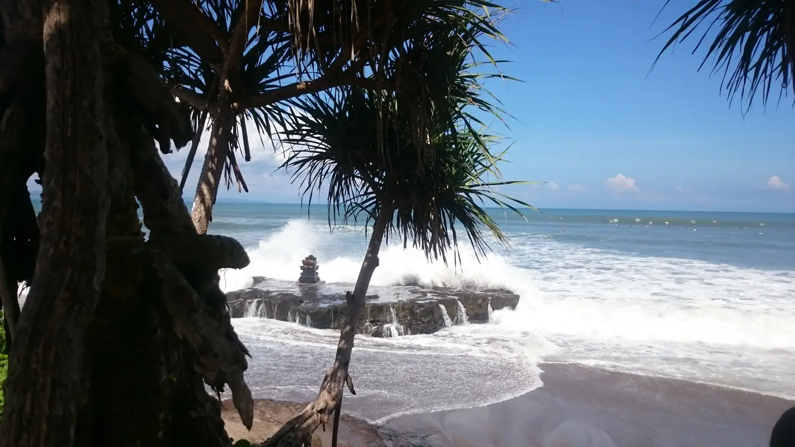 Waves breaking around a small shrine on a rock at the shoreline of Batu Bolong beach in Canggu