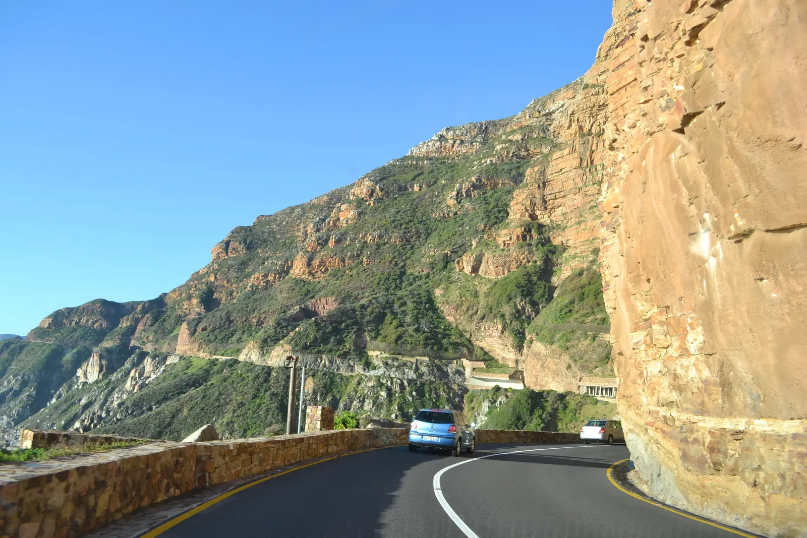 Chapman's Peak Drive curving under an overhanging sandstone cliff, with a stone wall on the sea side