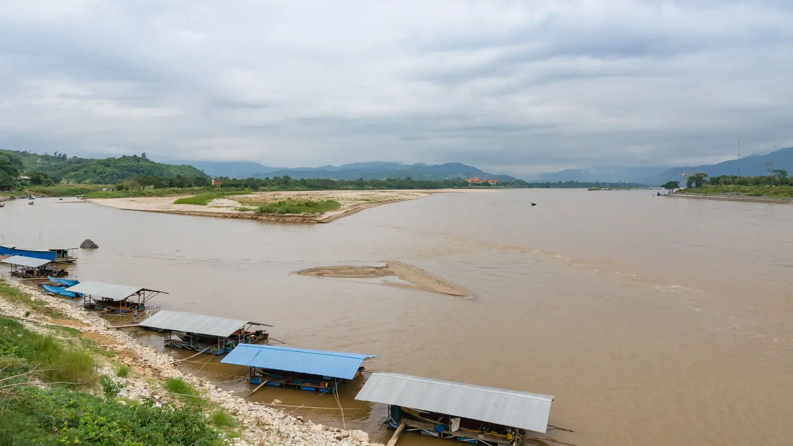 The wide brown Mekong at Sop Ruak with boat sheds on the Thai bank and hills beyond