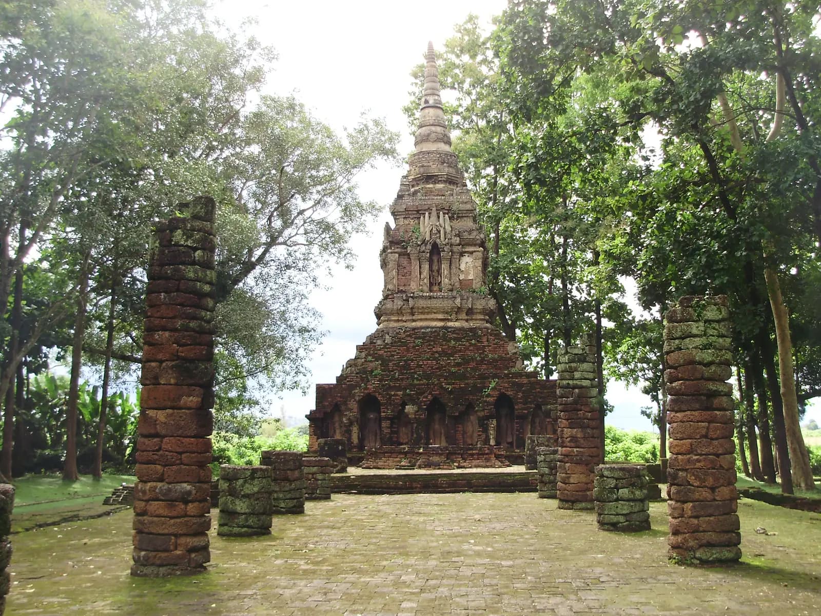 The old brick chedi of Wat Pa Sak framed by ruined pillars and trees