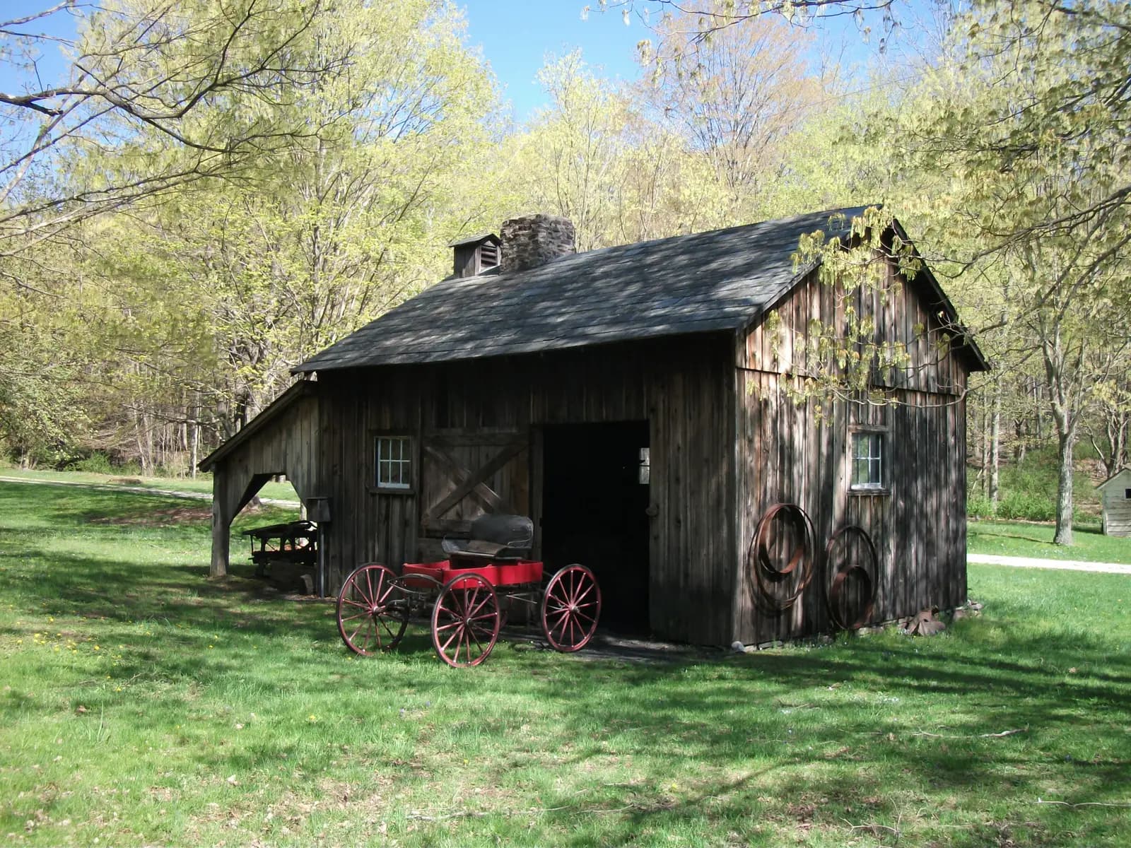 A weathered wooden barn with a red wagon on the grass at Millbrook Village