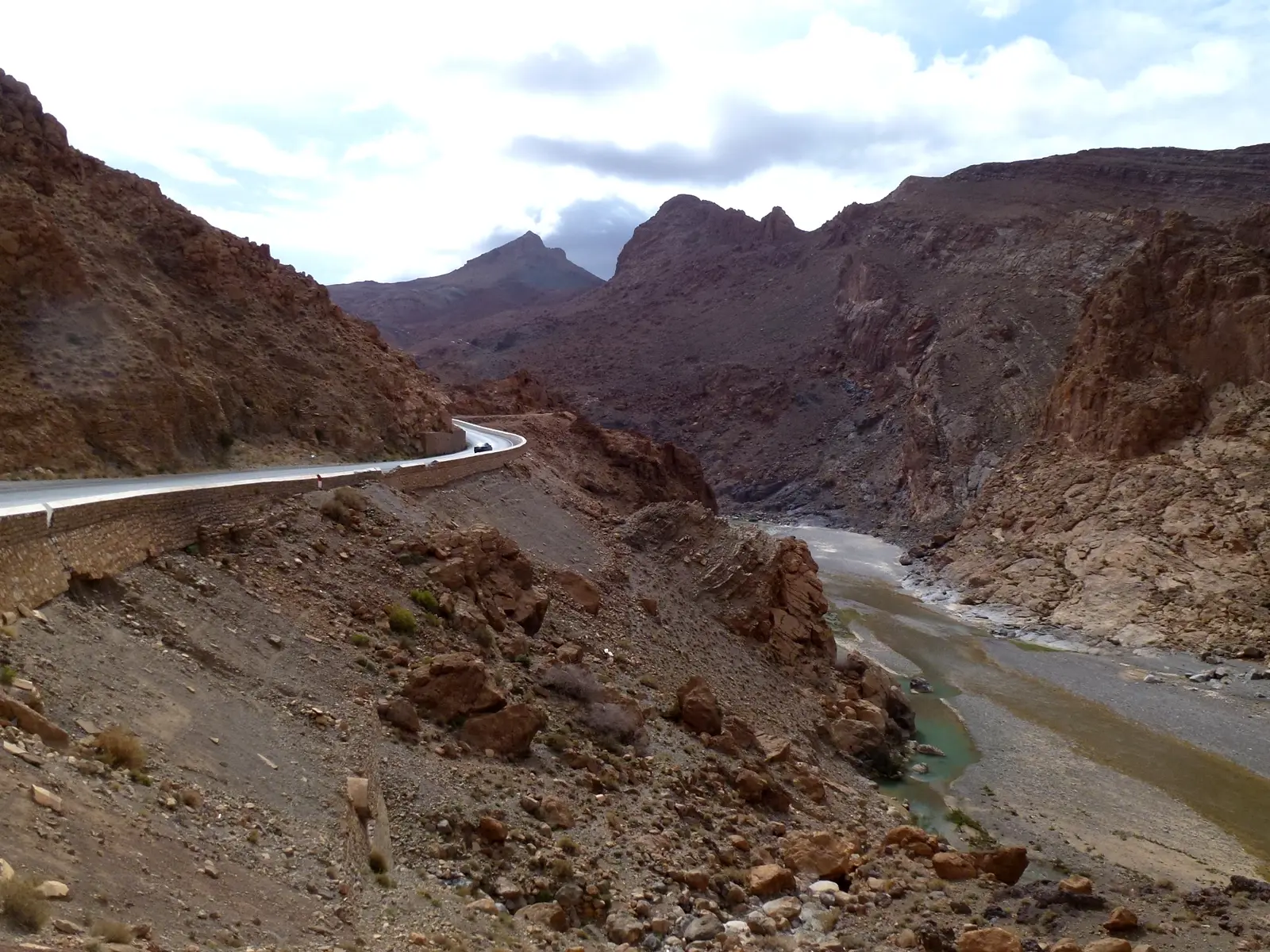 The N13 curving along a rocky slope above the Ziz river in the gorge, with jagged red mountains ahead