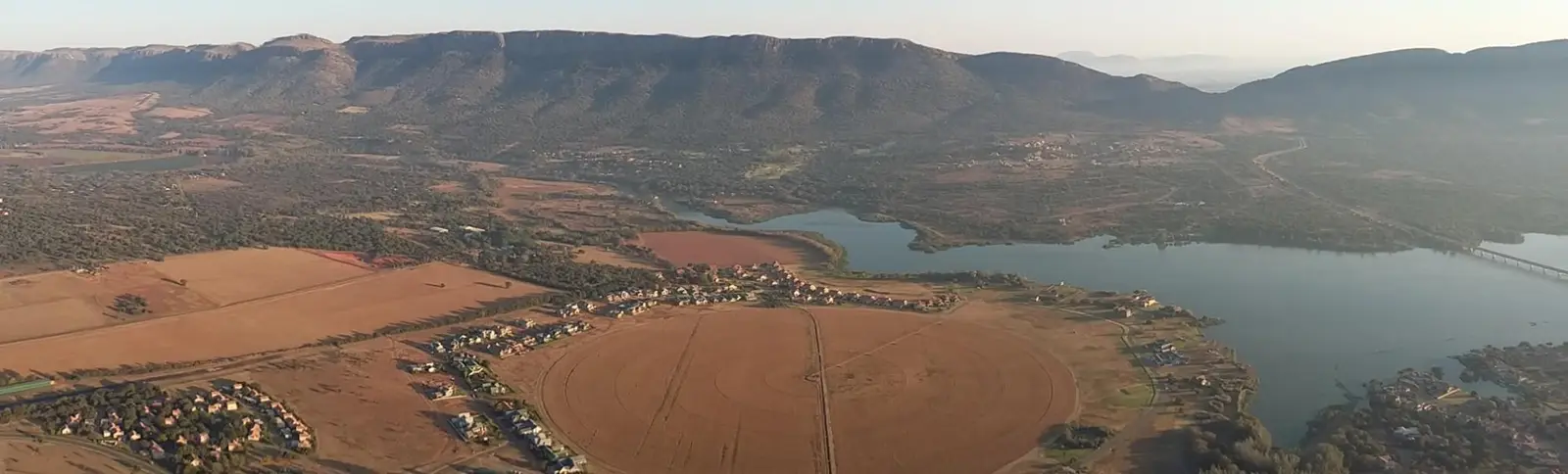 The Magaliesberg range at dawn above farmland and the western arm of the Hartbeespoort Dam, with the gap of Kommando Nek on the right