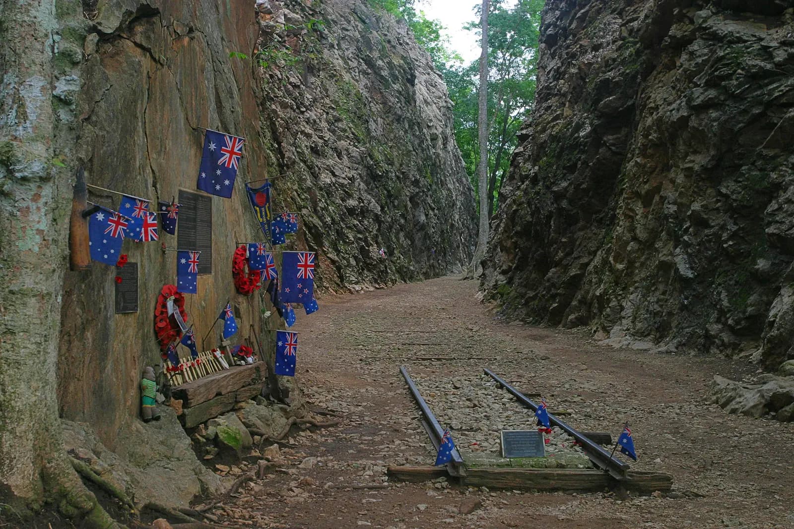 The deep rock cutting at Hellfire Pass, with a short length of railway track, flags and wreaths left against the rock wall
