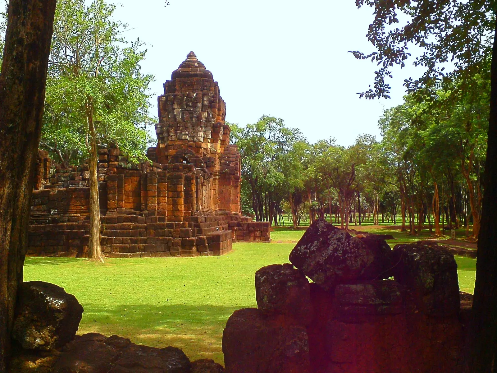 A laterite Khmer sanctuary tower rising above low walls on a green lawn at Prasat Mueang Sing
