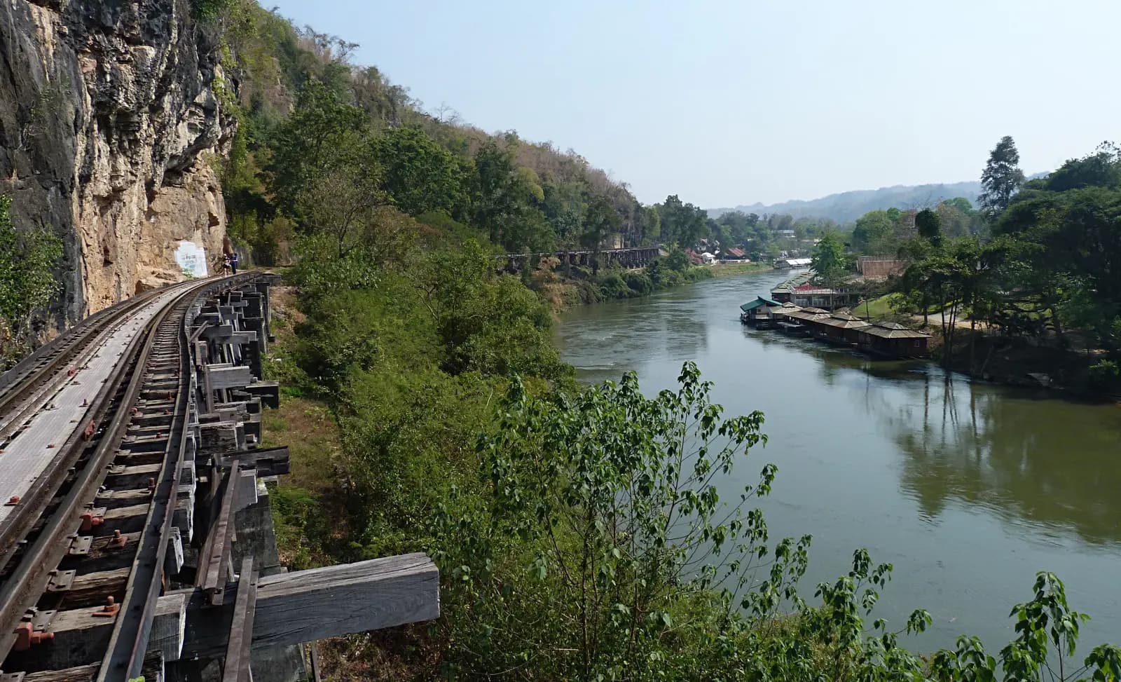The railway on its timber trestle beneath a limestone cliff, with the Khwae Noi river and floating houses below