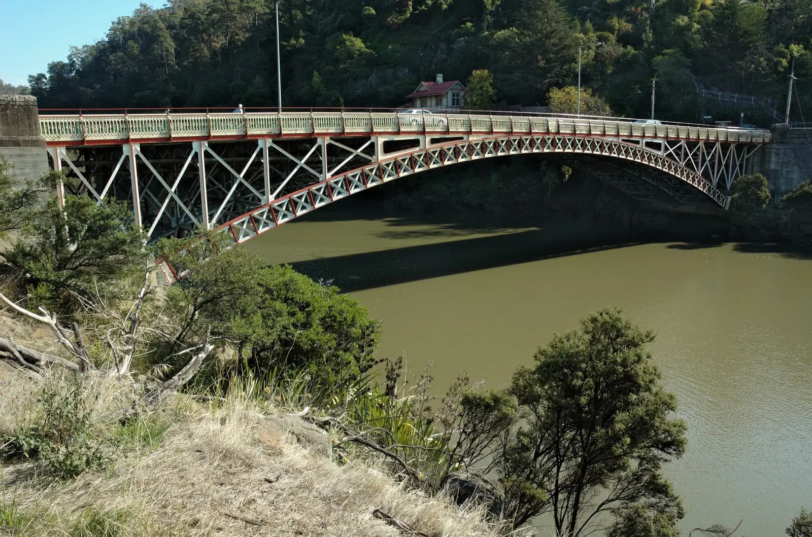 The red and cream iron arch of Kings Bridge over the river at the mouth of Cataract Gorge
