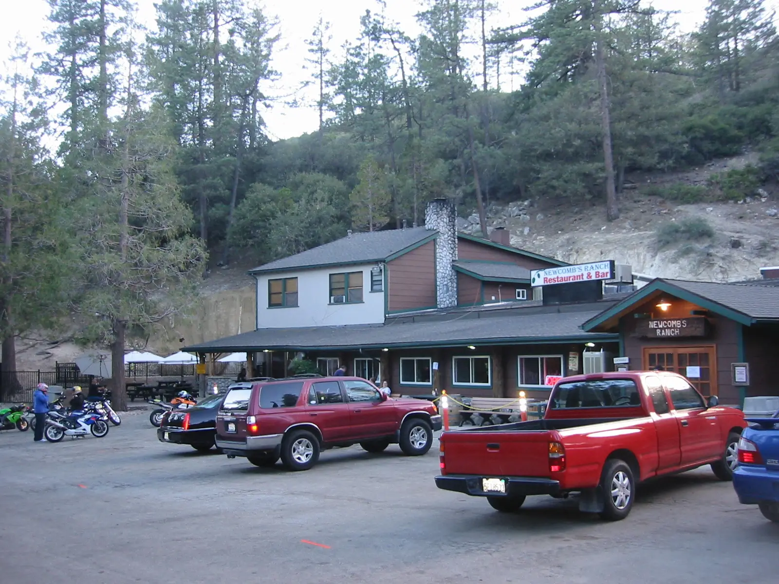 The Newcomb's Ranch roadhouse among pines, with motorcycles and pickups in the car park