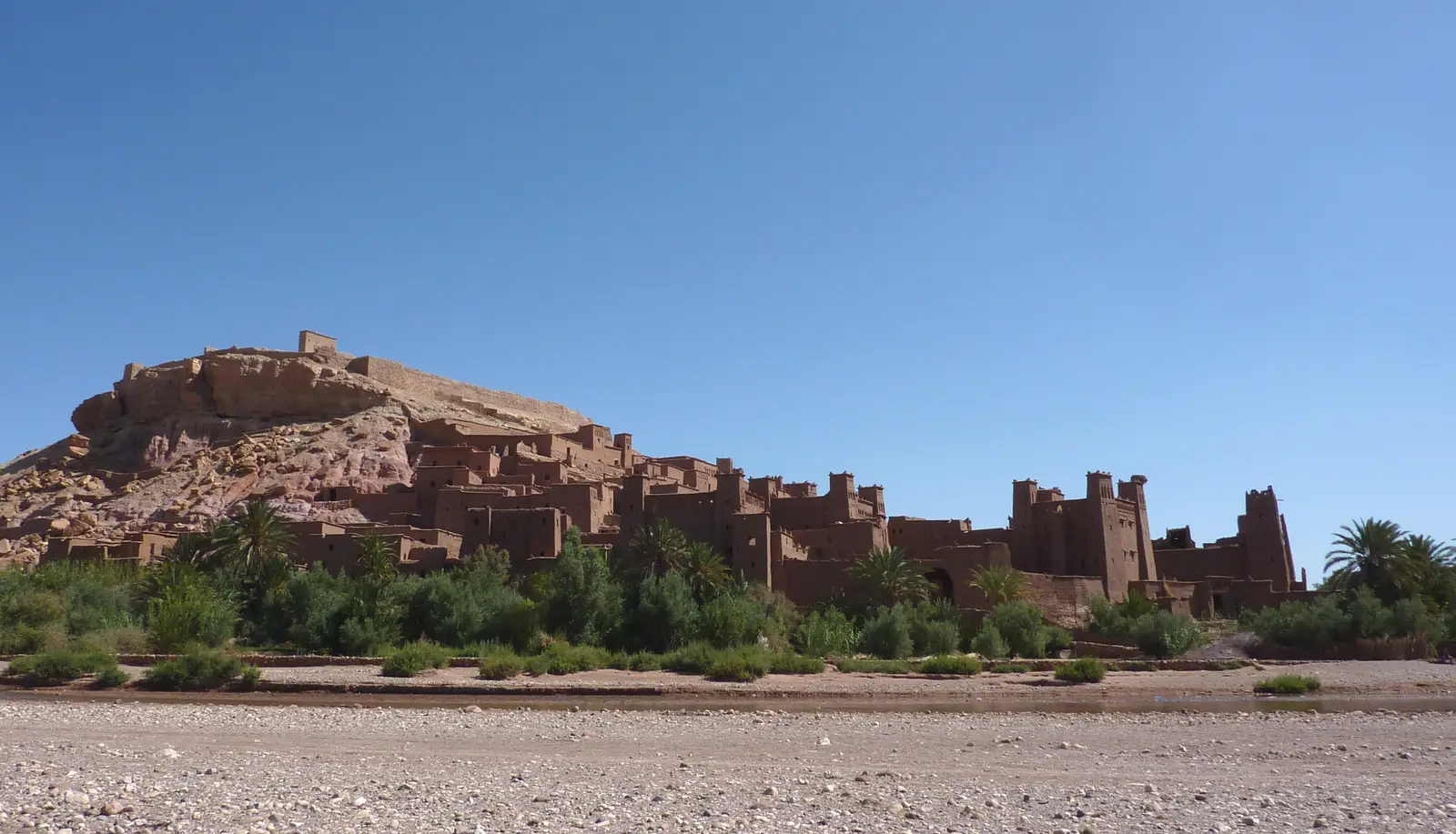 The ksar of Aït Benhaddou above a line of palms and the dry riverbed, in early morning light