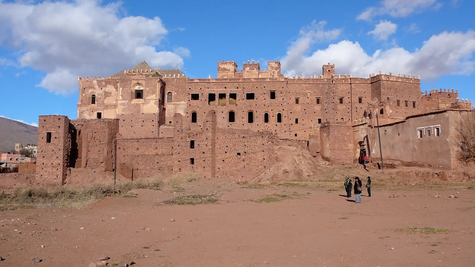 The long earthen facade of Telouet Kasbah under a blue sky with white clouds