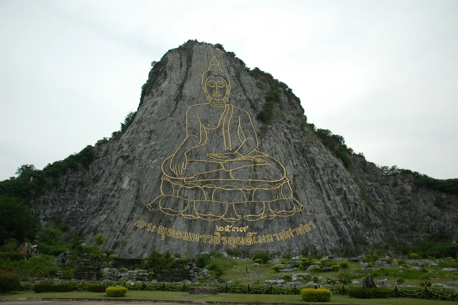 The gold outline of a seated Buddha etched into the cliff face of Khao Chi Chan, above a lawn and gardens