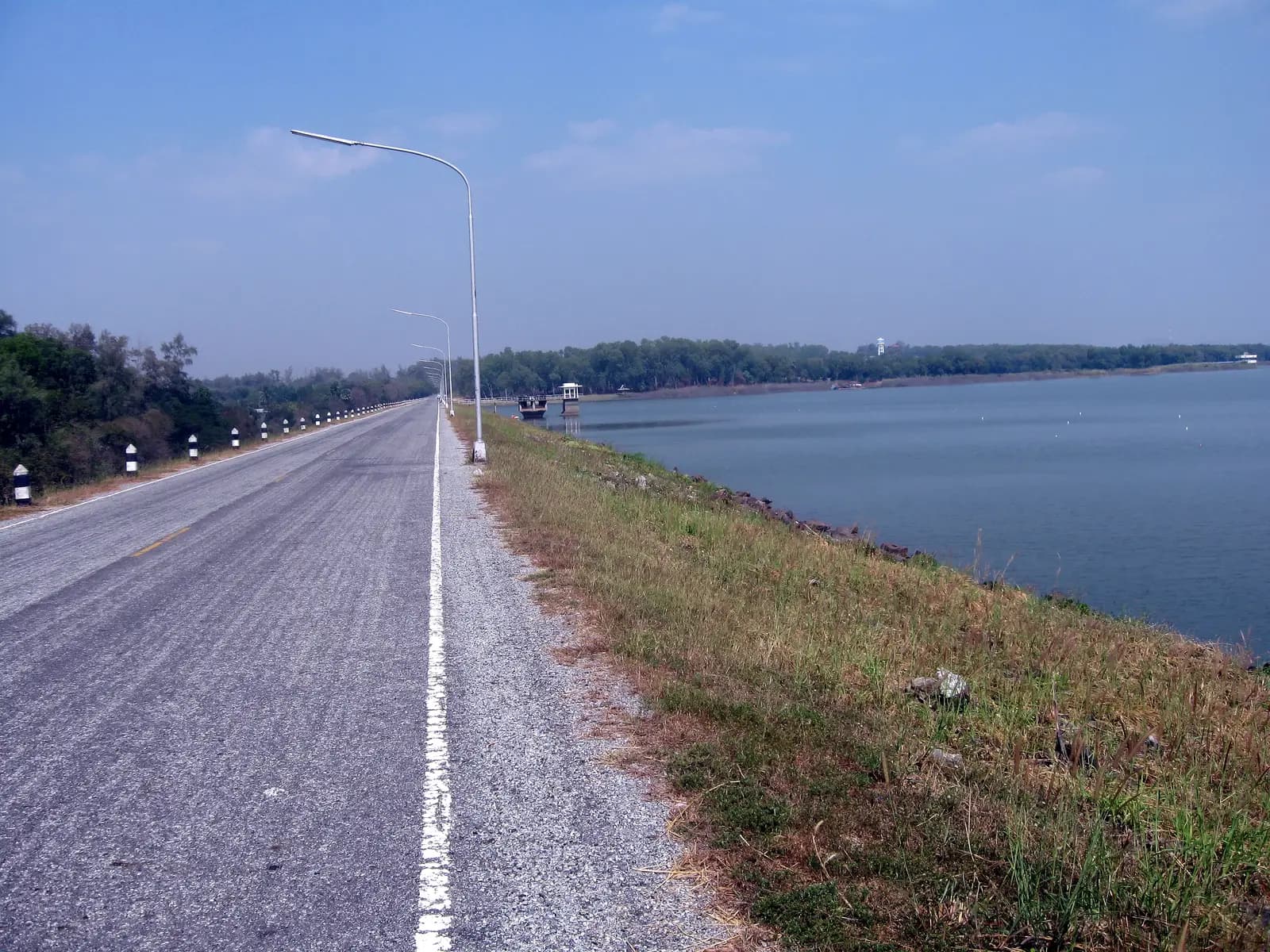 A paved road with street lamps running beside the water of Mabprachan Reservoir
