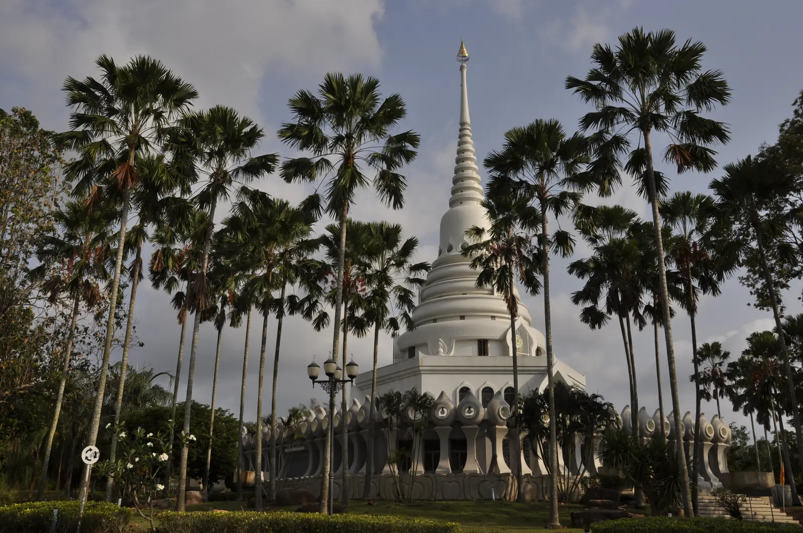 A tall white chedi framed by palm trees at Wat Yansangwararam