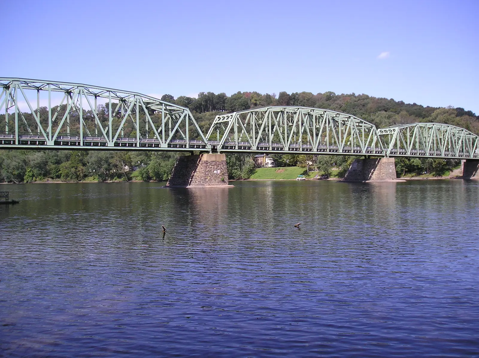 The green steel truss spans of the Upper Black Eddy–Milford Bridge over the Delaware, with wooded hills behind