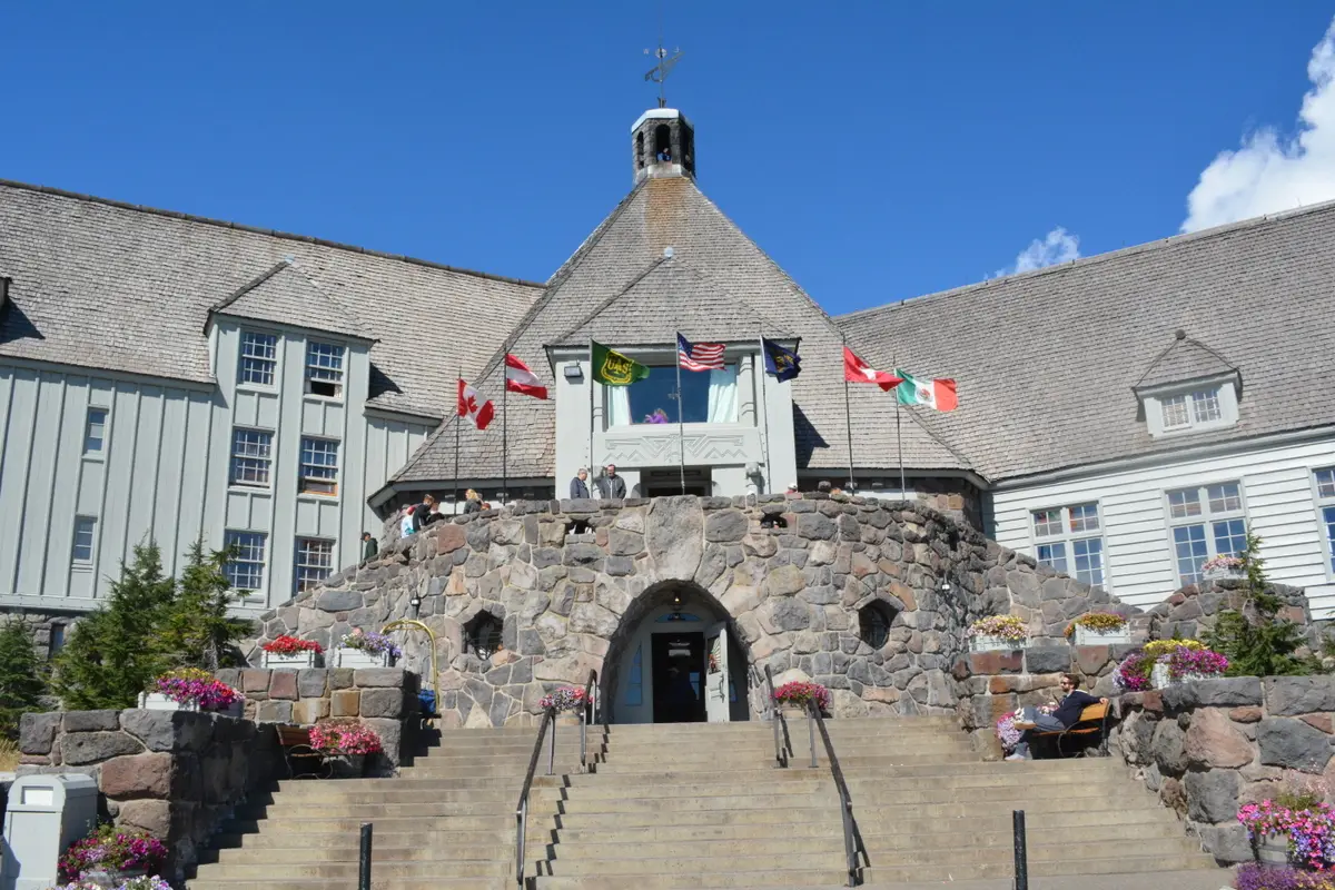The front of Timberline Lodge, a stone and timber building with a steep shingled roof, under a blue sky