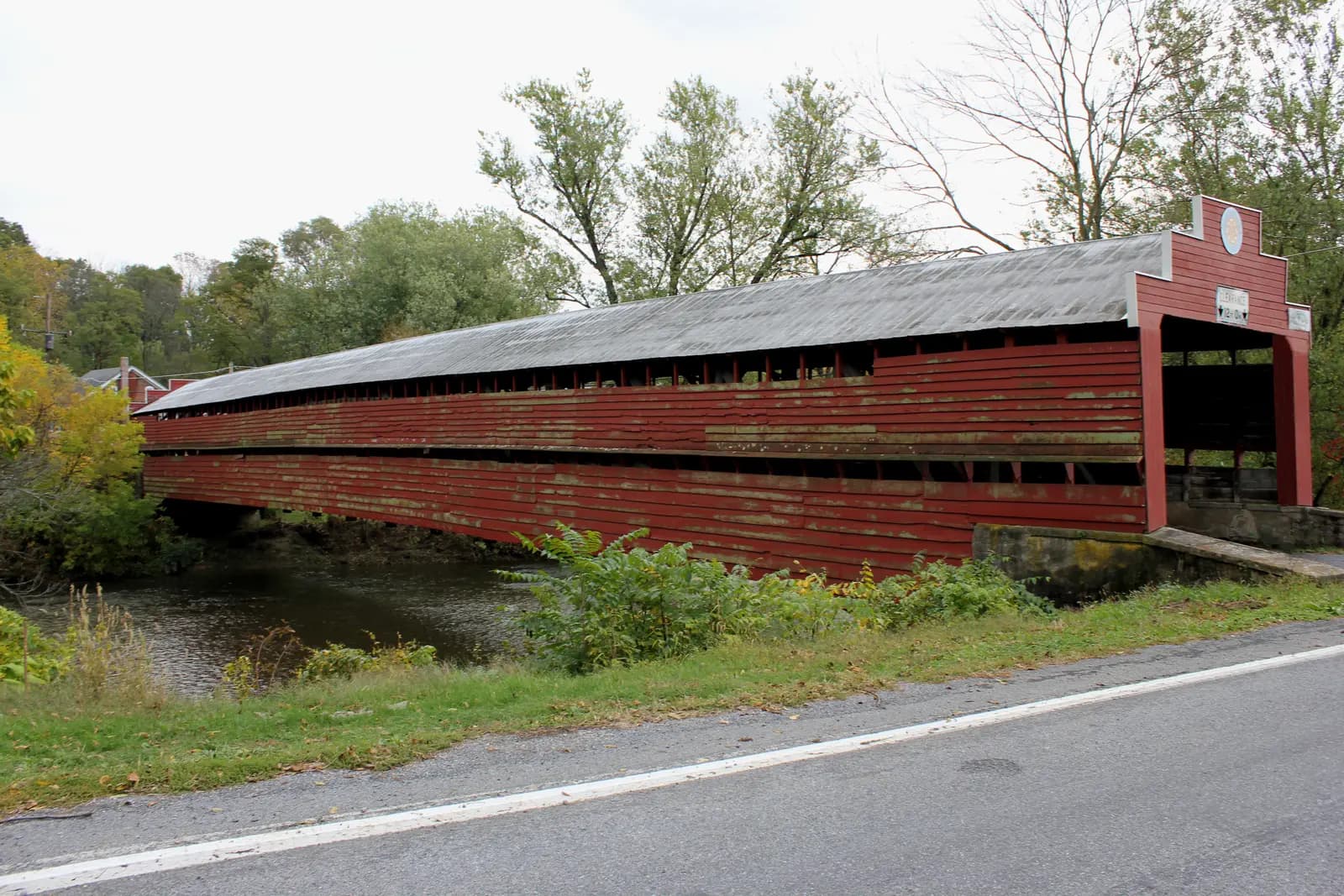 The long red Dreibelbis Station covered bridge across Maiden Creek, with autumn trees behind
