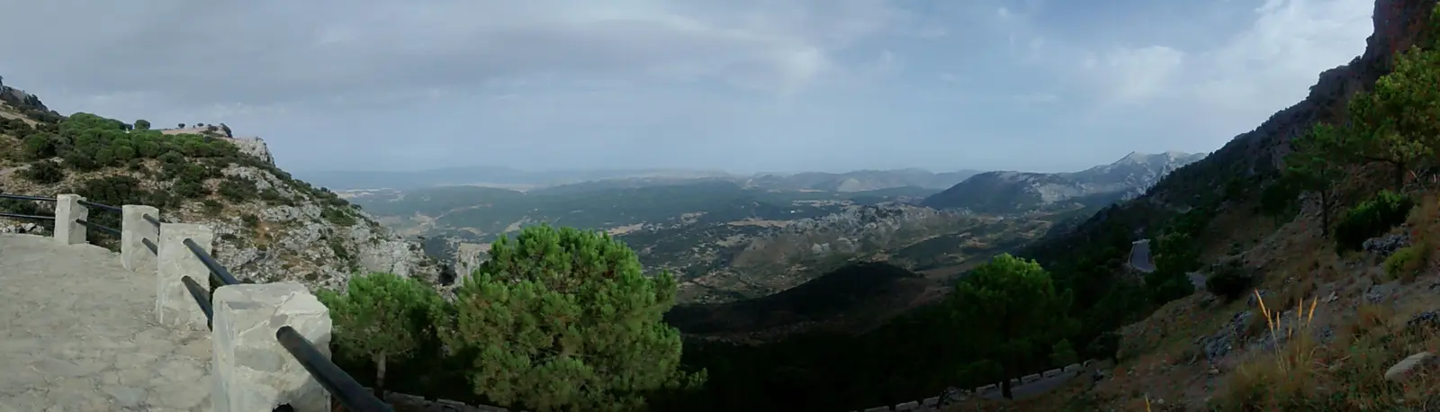 Panorama from the stone-railed viewpoint at the Puerto de las Palomas over pine-covered slopes and distant mountain ranges
