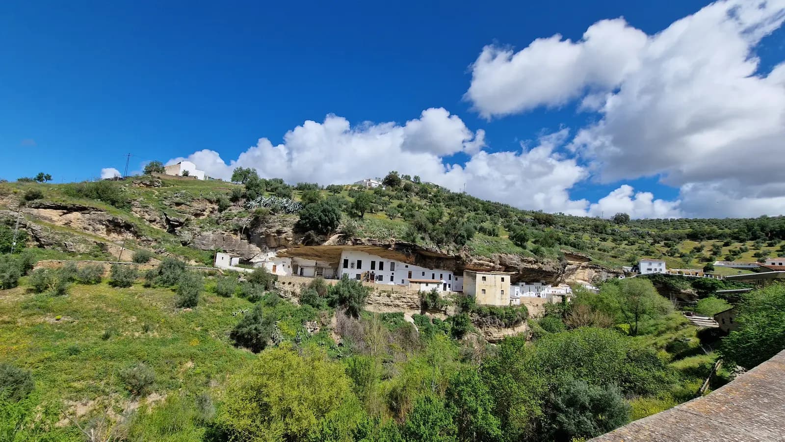 White houses built under a long overhang of rock above the green valley at Setenil de las Bodegas