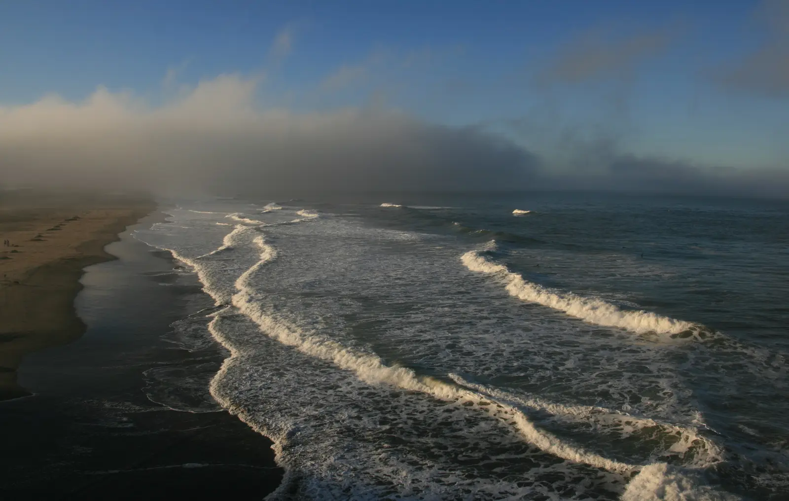 Surf rolling onto Ocean Beach as a bank of fog lifts off the sea