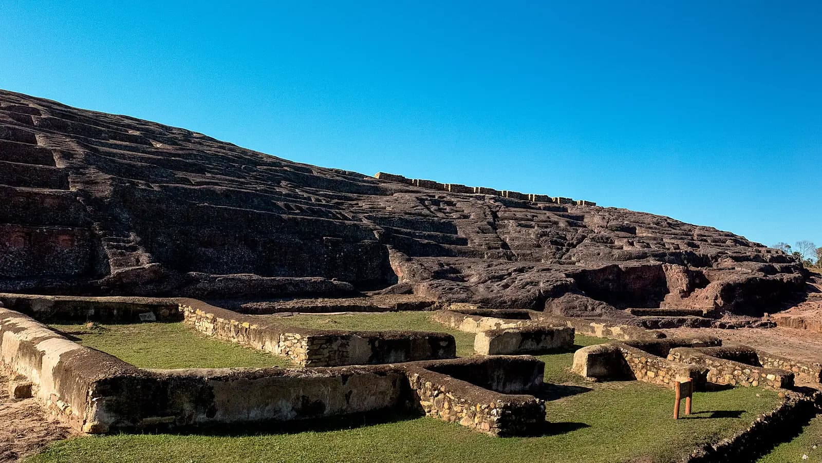 The carved sandstone ridge of El Fuerte above the stone foundations of later buildings, under a clear blue sky
