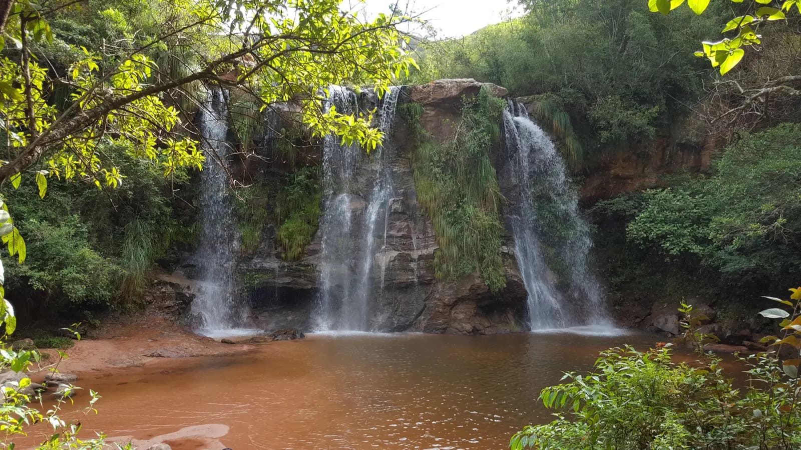 Water falling in several streams over a rock face into a brown pool at Las Cuevas