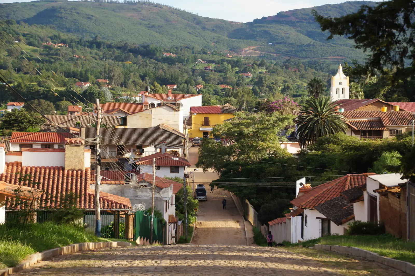 A cobbled street in Samaipata running down between tiled roofs towards a white church tower and green hills