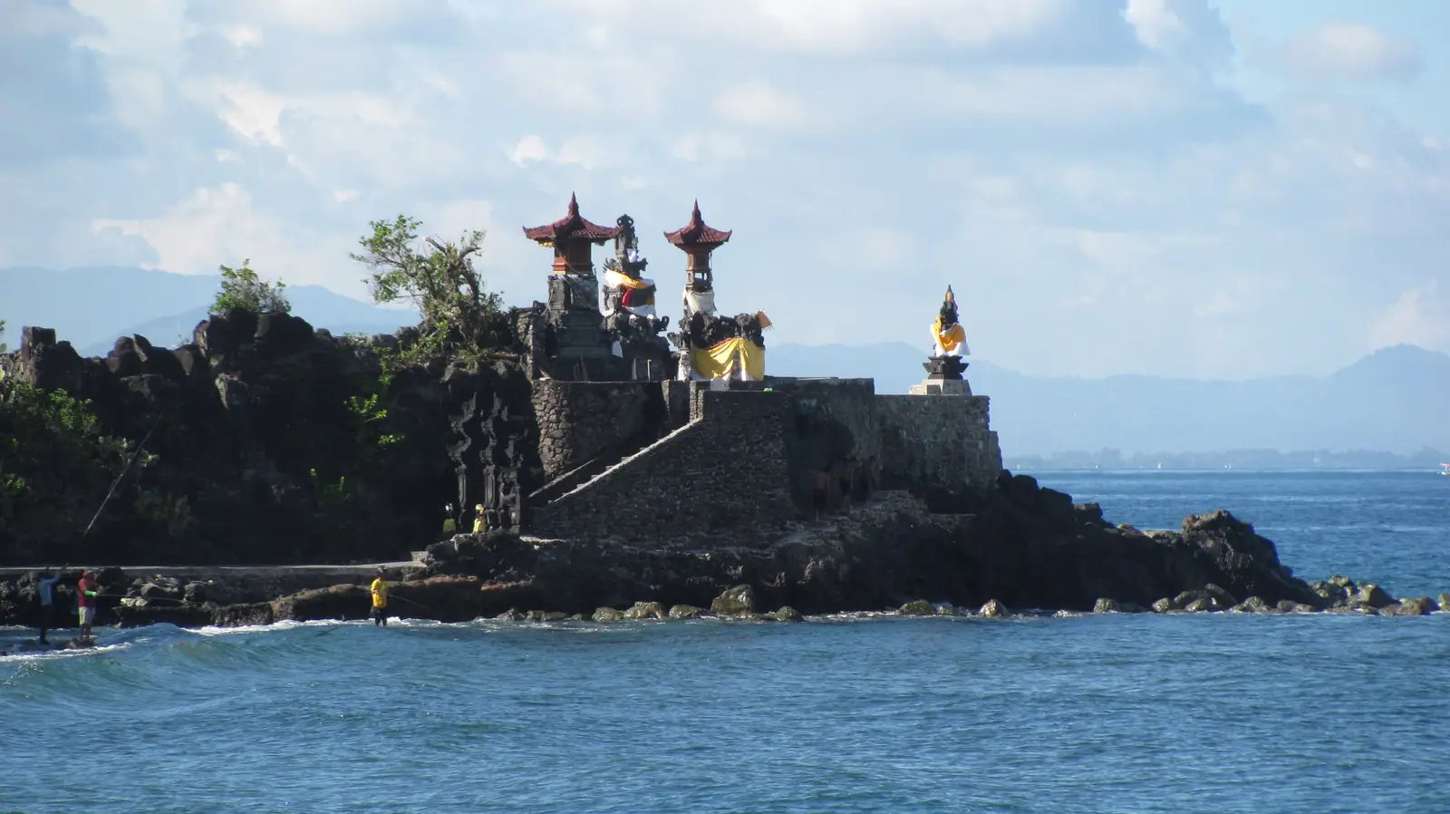 The shrines and gateways of Pura Batu Bolong on a black rock point running out into the sea