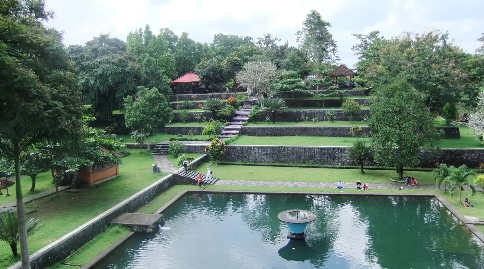 Terraced lawns and garden pavilions rising above a green pool with a fountain at Taman Narmada
