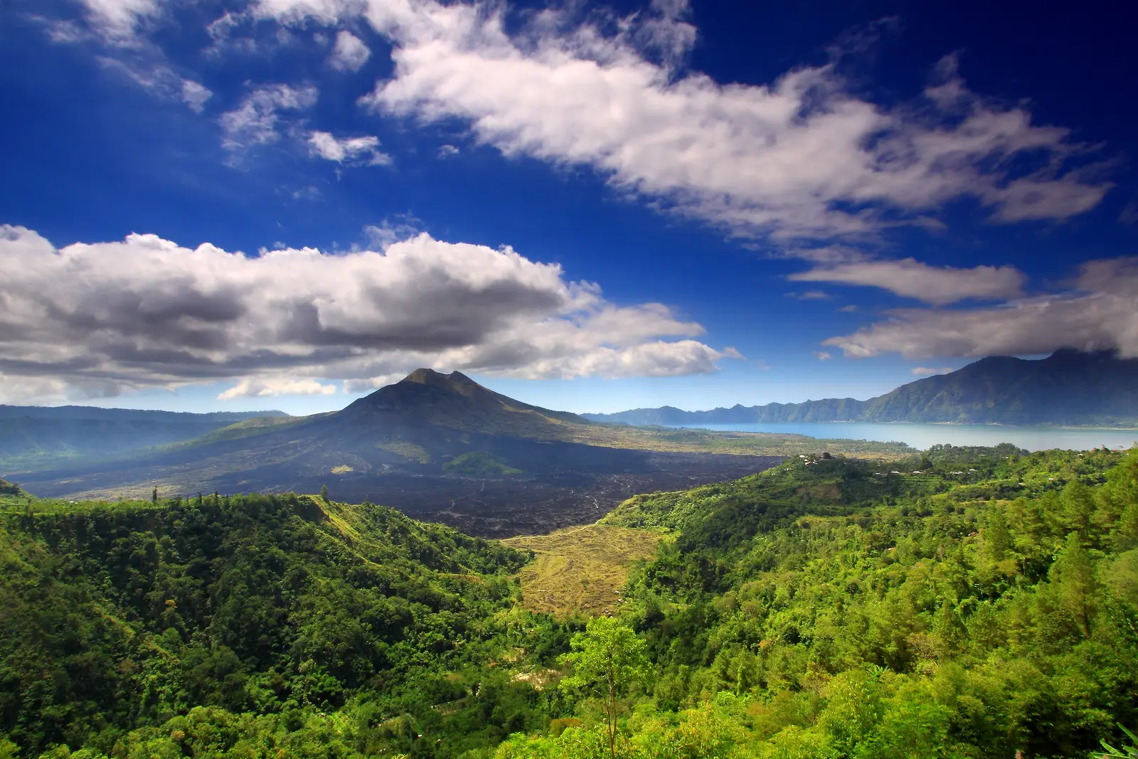 Mount Batur and the lake below it, seen across forested slopes from the caldera rim
