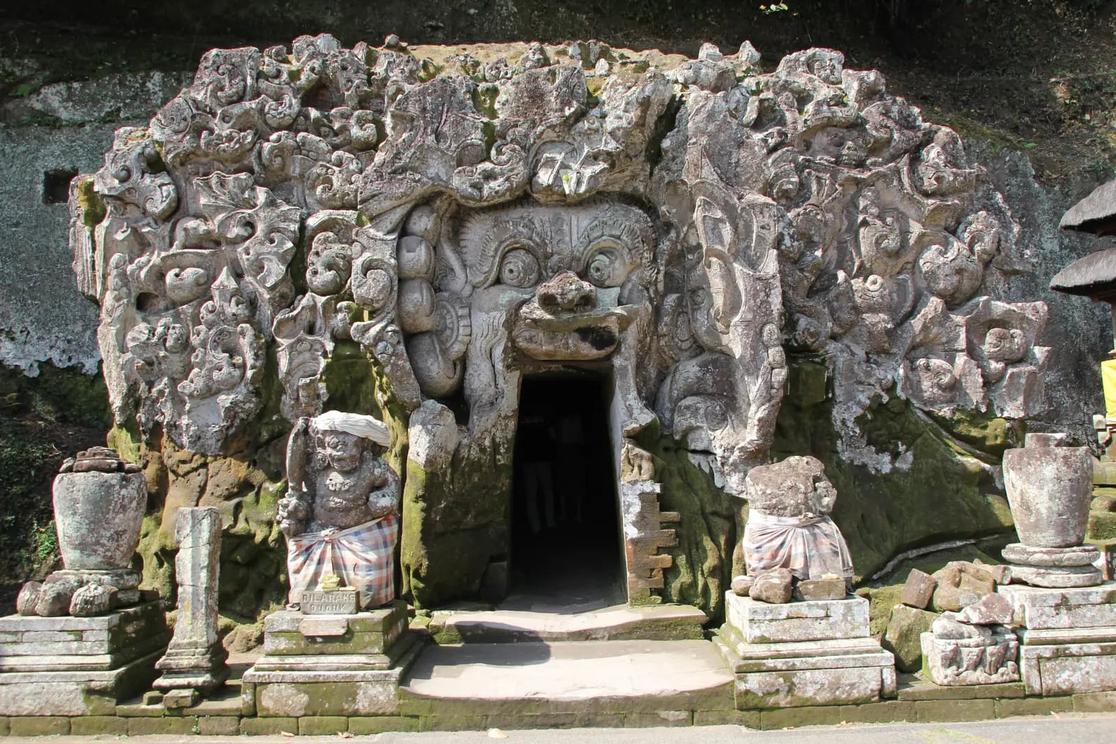 The carved stone face around the cave entrance at Goa Gajah, flanked by statues