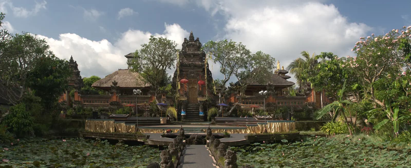 A walkway between lotus ponds leading to the carved red-brick gate of Pura Taman Saraswati