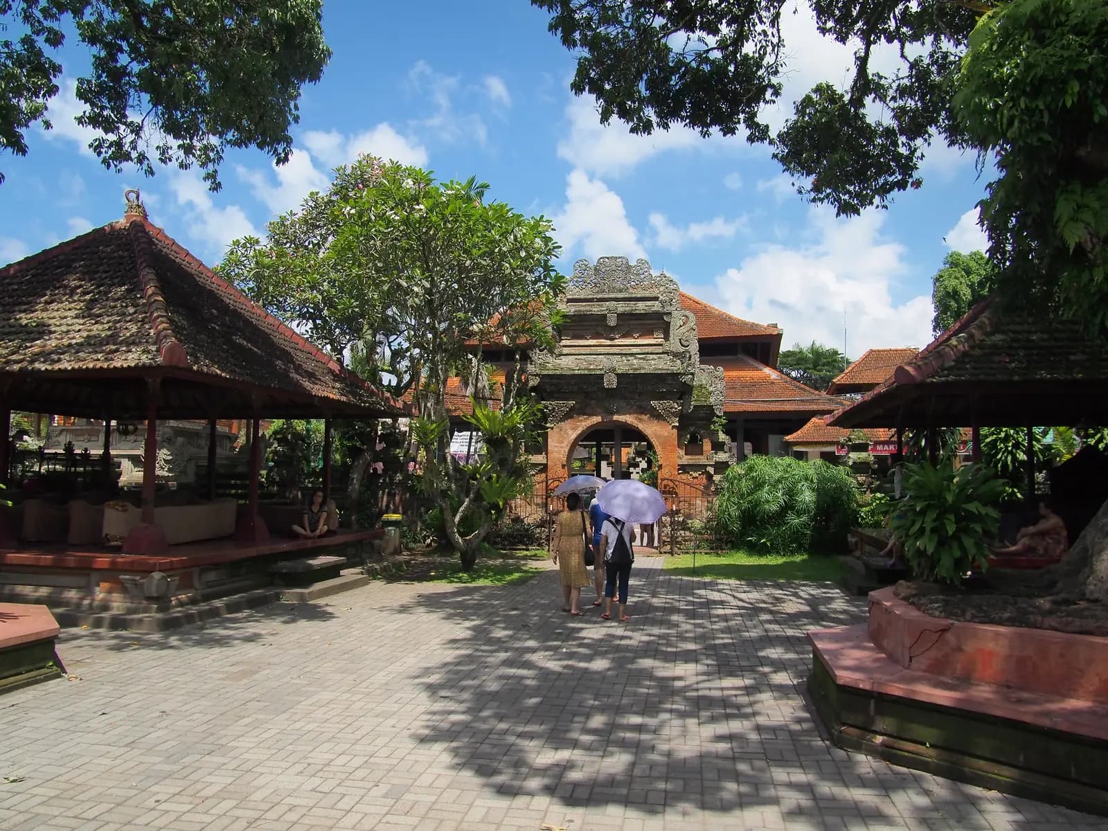 The paved courtyard of Ubud Palace with a carved stone gateway and thatched pavilions